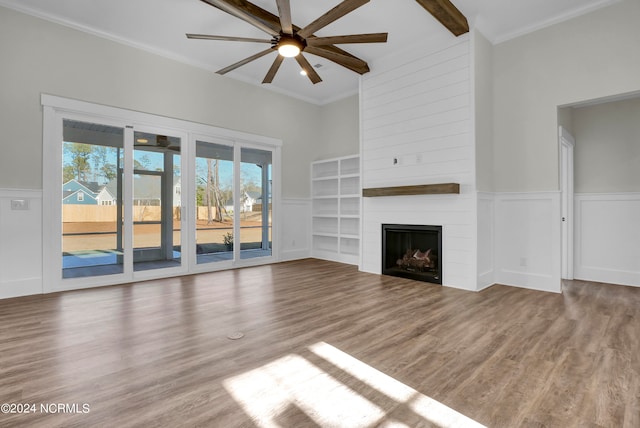 unfurnished living room with a fireplace, wood finished floors, a ceiling fan, and a wainscoted wall