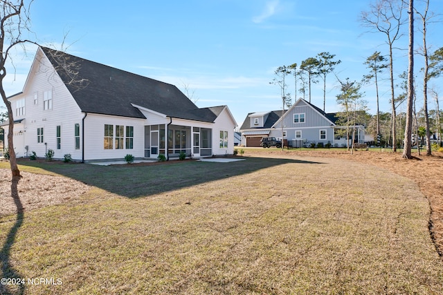 back of property featuring a lawn, a shingled roof, and a sunroom