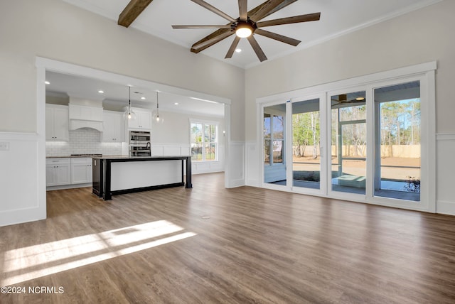 unfurnished living room featuring a ceiling fan, a wainscoted wall, light wood-style flooring, crown molding, and a decorative wall