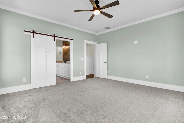 unfurnished bedroom featuring ensuite bathroom, a barn door, ceiling fan, crown molding, and light colored carpet