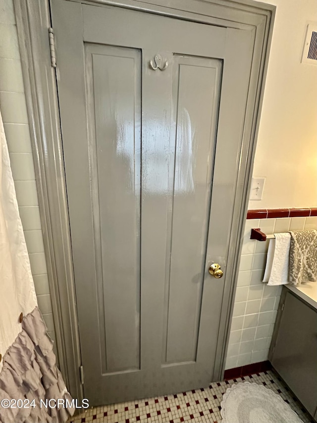 bathroom with visible vents, wainscoting, tile patterned floors, vanity, and tile walls