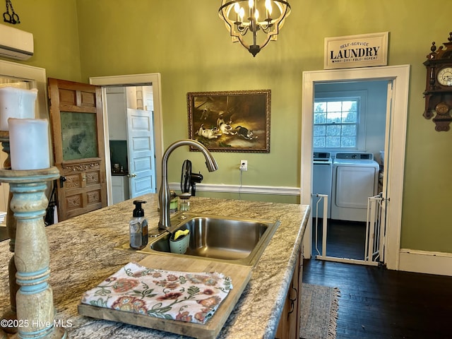 kitchen with a sink, a wall mounted AC, dark wood-style floors, washer and clothes dryer, and pendant lighting