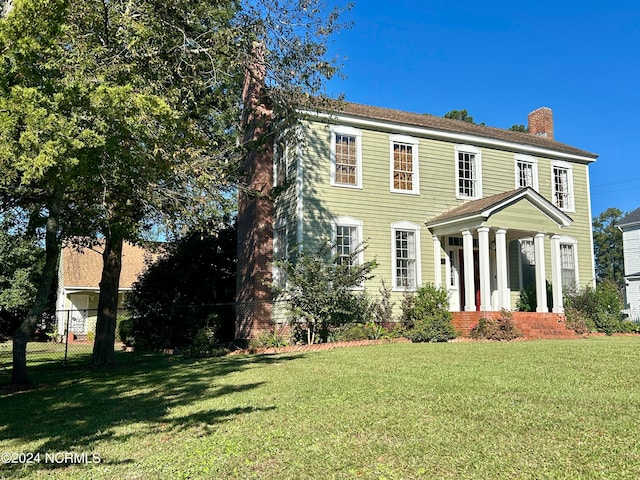 colonial home with a chimney, fence, and a front lawn