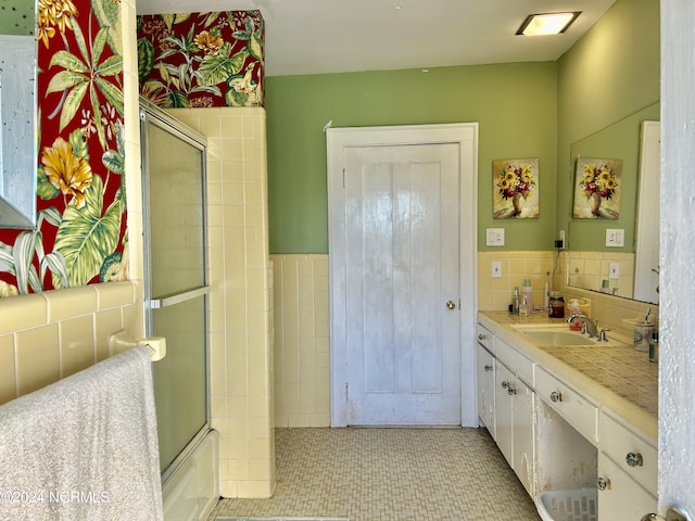 bathroom featuring a wainscoted wall, shower / bath combination with glass door, tile walls, and vanity