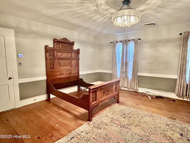 bedroom with baseboards, a notable chandelier, visible vents, and wood finished floors