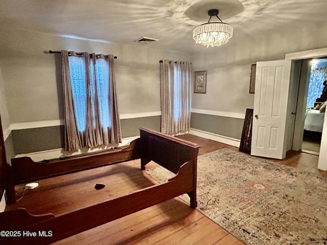 unfurnished bedroom featuring a chandelier, wood finished floors, visible vents, and baseboards