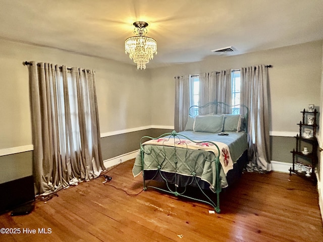 bedroom featuring visible vents, a notable chandelier, baseboards, and wood finished floors