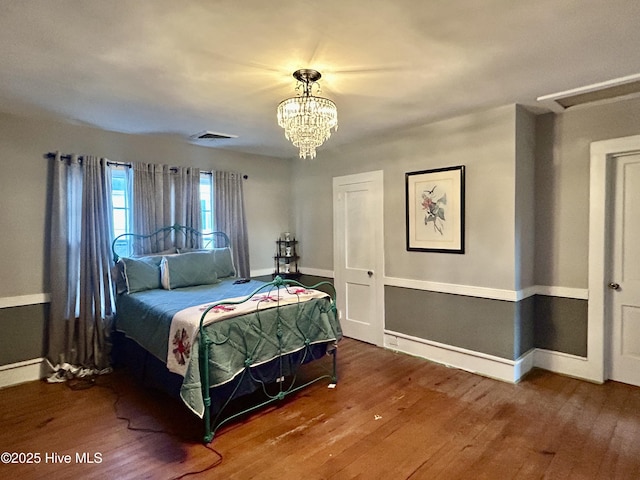 bedroom with an inviting chandelier, visible vents, baseboards, and wood finished floors