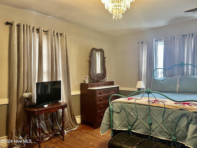 bedroom featuring baseboards, visible vents, an inviting chandelier, and wood finished floors