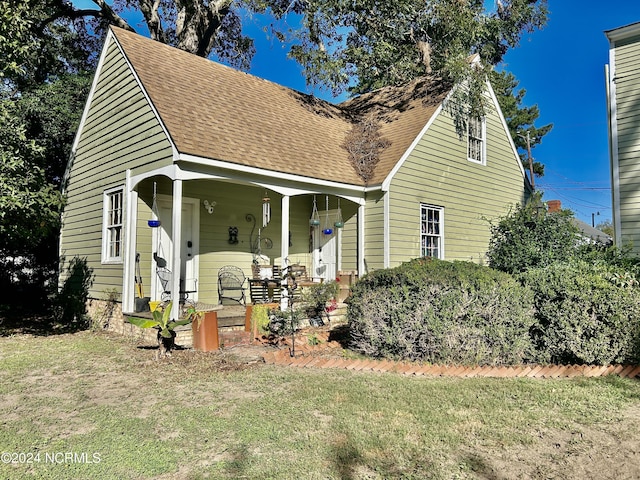 cape cod home featuring a shingled roof, a front yard, and a porch