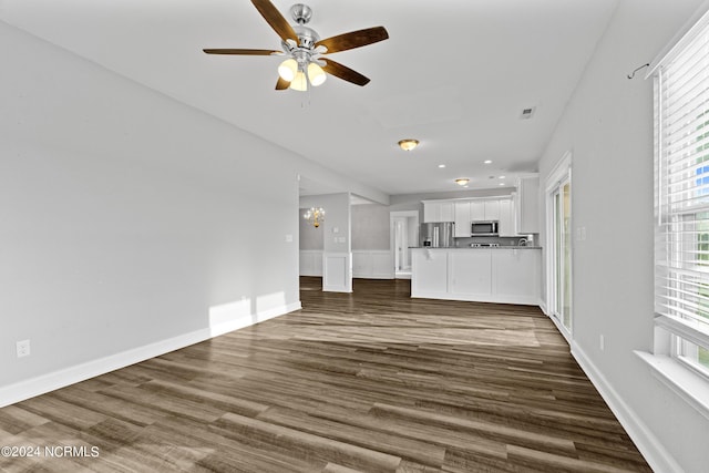 unfurnished living room featuring dark wood-type flooring and ceiling fan with notable chandelier