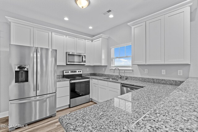 kitchen featuring a notable chandelier, sink, light stone countertops, appliances with stainless steel finishes, and white cabinetry