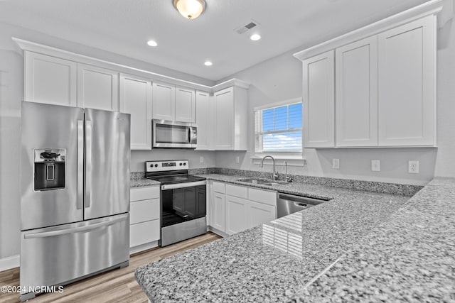 kitchen featuring white cabinetry, sink, light hardwood / wood-style floors, stainless steel appliances, and light stone countertops