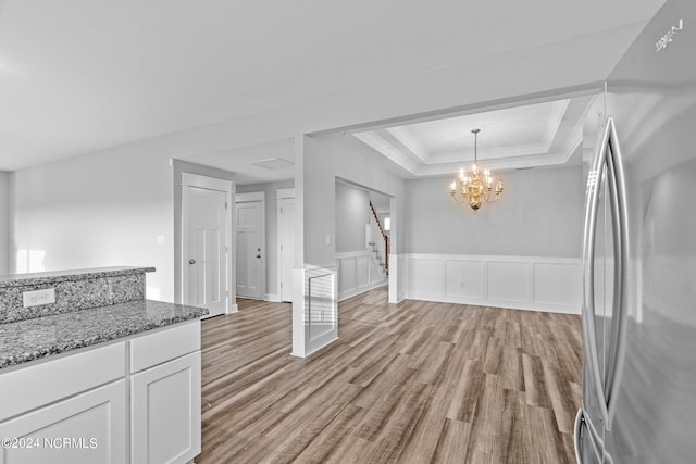 kitchen featuring light wood-type flooring, hanging light fixtures, white cabinetry, stainless steel refrigerator, and dark stone counters