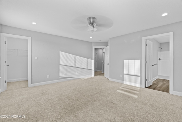 unfurnished bedroom featuring ensuite bathroom, a walk in closet, a closet, ceiling fan, and carpet