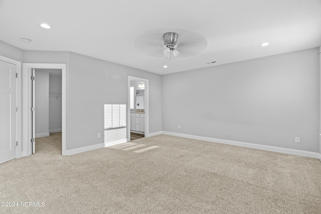 unfurnished bedroom with ensuite bathroom, a spacious closet, ceiling fan, light carpet, and a closet