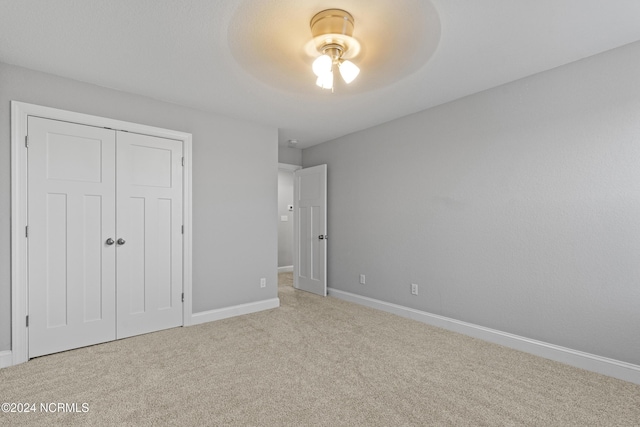 unfurnished bedroom with light carpet, ceiling fan, and a closet