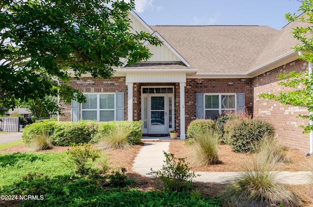 doorway to property featuring brick siding, board and batten siding, and a shingled roof