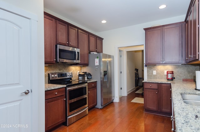 kitchen featuring light stone counters, backsplash, appliances with stainless steel finishes, and dark hardwood / wood-style floors