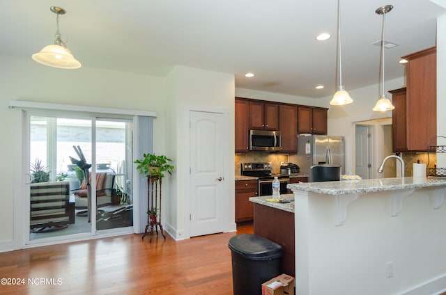 kitchen featuring light hardwood / wood-style flooring, decorative light fixtures, light stone counters, backsplash, and appliances with stainless steel finishes