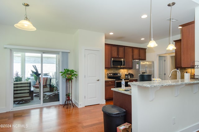 kitchen with light wood-style floors, tasteful backsplash, a breakfast bar area, a peninsula, and appliances with stainless steel finishes