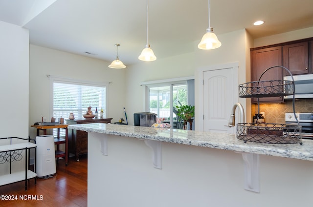 kitchen with a healthy amount of sunlight, light stone countertops, dark hardwood / wood-style flooring, and a breakfast bar