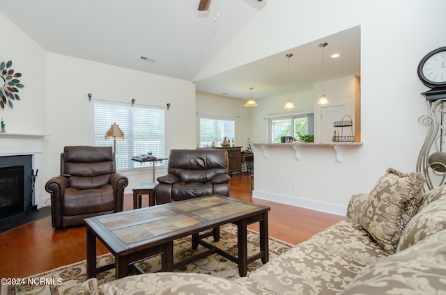 living area featuring lofted ceiling, a fireplace with flush hearth, visible vents, wood finished floors, and a ceiling fan