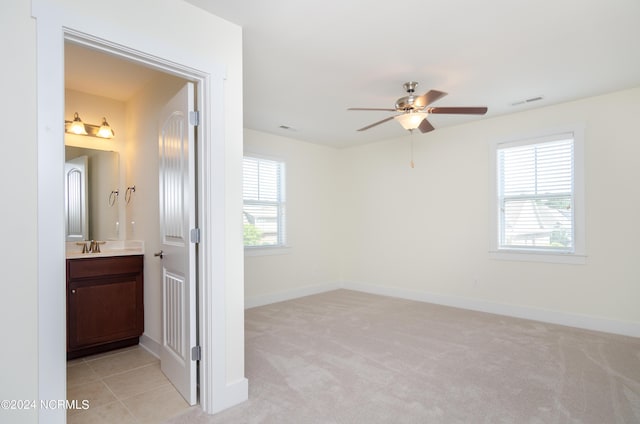 unfurnished bedroom with baseboards, multiple windows, light colored carpet, and a sink