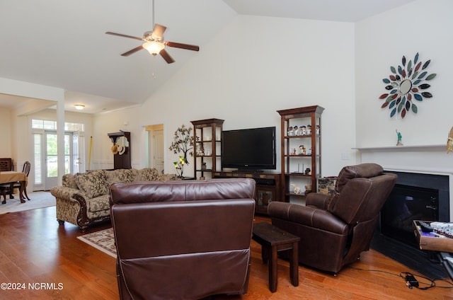 living room with high vaulted ceiling, wood finished floors, a ceiling fan, and a glass covered fireplace