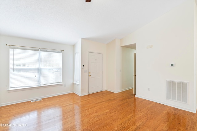 unfurnished room featuring lofted ceiling, a textured ceiling, and light wood-type flooring