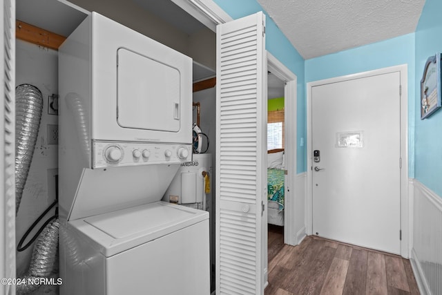 laundry area featuring dark wood-type flooring, electric water heater, stacked washer / drying machine, and a textured ceiling