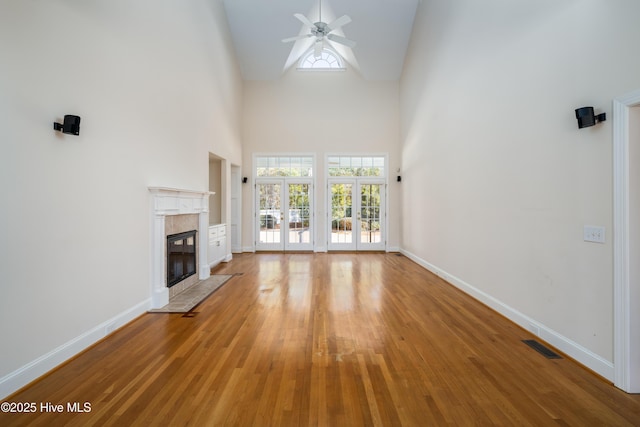 unfurnished living room with a tile fireplace, high vaulted ceiling, ceiling fan, and light hardwood / wood-style floors