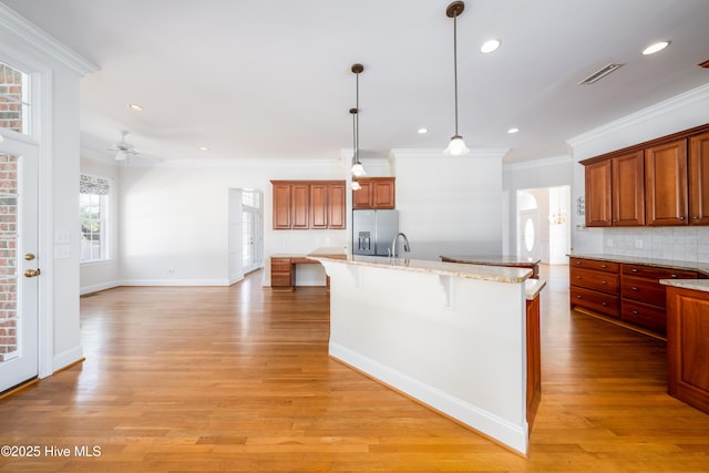 kitchen featuring a kitchen bar, hanging light fixtures, light wood-type flooring, stainless steel fridge, and a kitchen island with sink