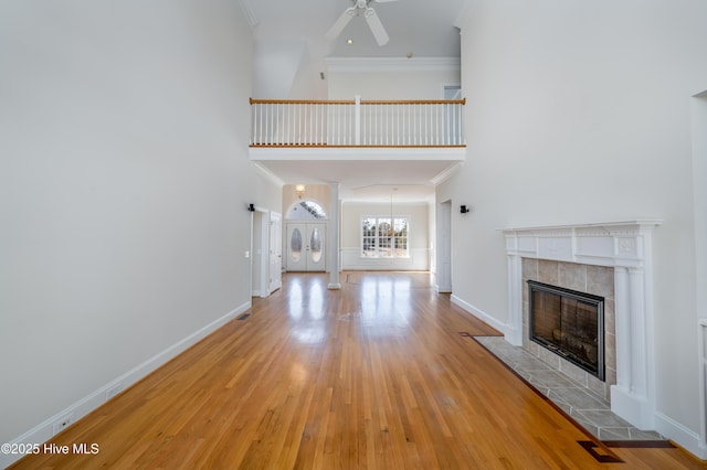 unfurnished living room featuring ornamental molding, a towering ceiling, a fireplace, and light hardwood / wood-style flooring