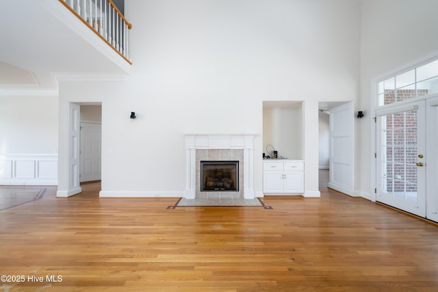 unfurnished living room featuring a towering ceiling, ornamental molding, a tile fireplace, and light wood-type flooring