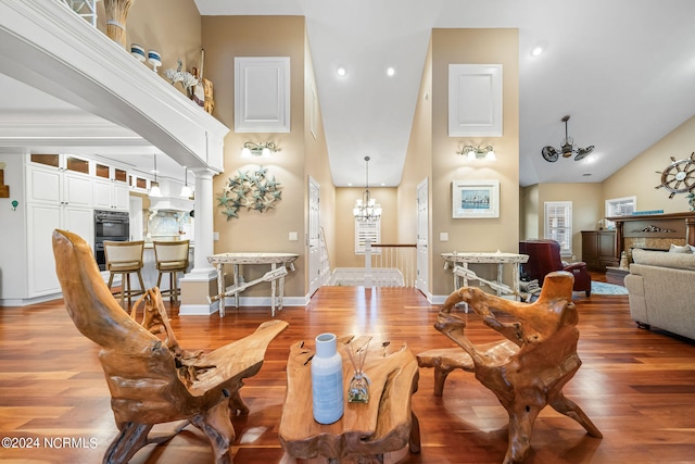 dining area featuring high vaulted ceiling, decorative columns, wood-type flooring, and a chandelier