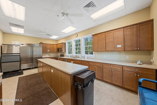 kitchen with appliances with stainless steel finishes, sink, light tile patterned flooring, a center island, and ceiling fan