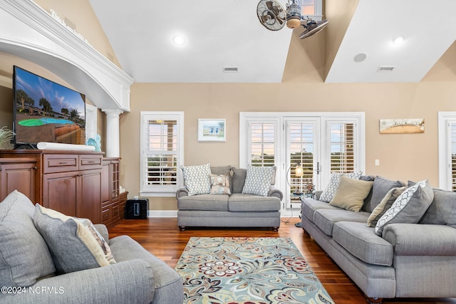 living room featuring dark wood-type flooring, vaulted ceiling, decorative columns, and a wealth of natural light