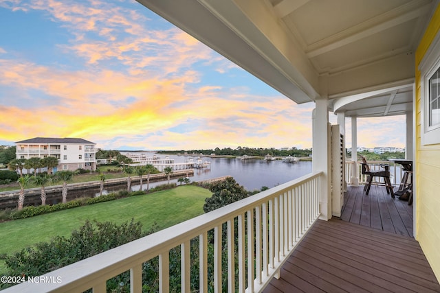 deck at dusk featuring a water view and a lawn