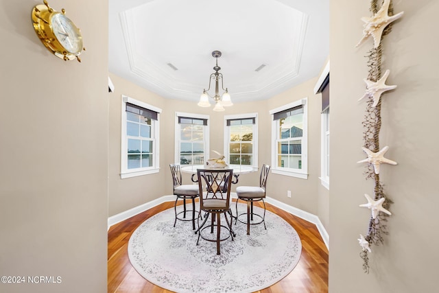 dining space with ornamental molding, hardwood / wood-style floors, a notable chandelier, and a tray ceiling