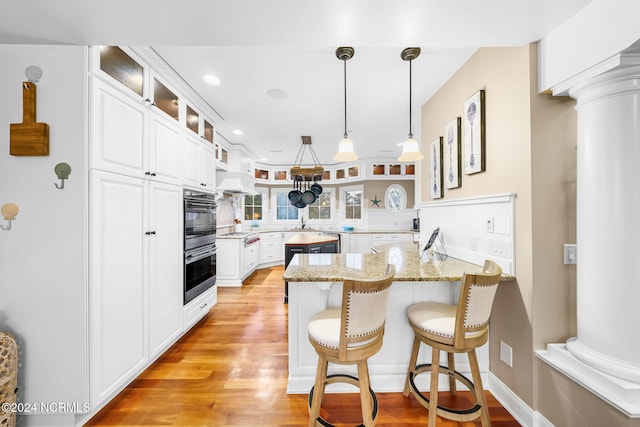 kitchen with light stone counters, white cabinetry, kitchen peninsula, and ornate columns