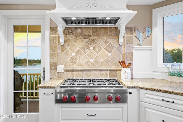 kitchen with tasteful backsplash, white cabinetry, stainless steel gas cooktop, ventilation hood, and a water view