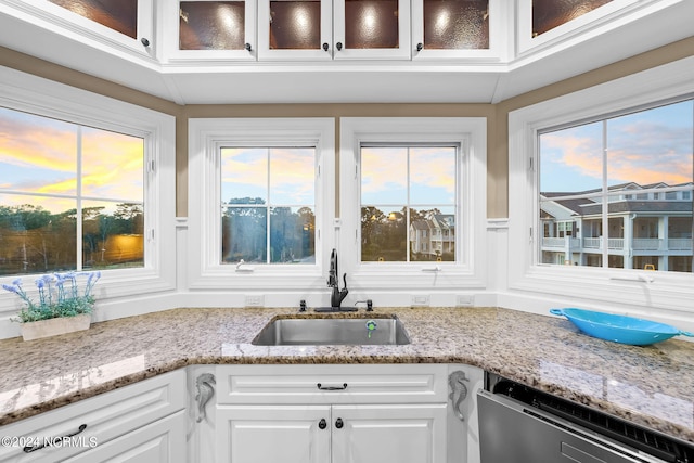 kitchen with stainless steel dishwasher, sink, white cabinetry, and light stone counters