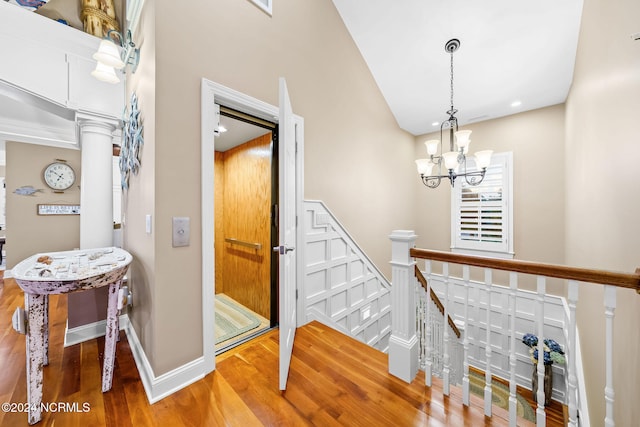 stairs with a chandelier, wood-type flooring, and decorative columns