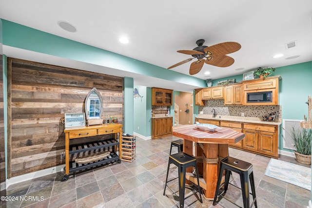 kitchen with black microwave, tasteful backsplash, ceiling fan, wood walls, and sink