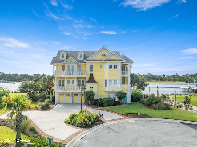 view of front facade with a front lawn, a garage, a water view, and a balcony