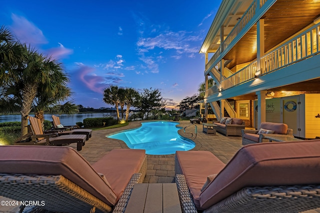 pool at dusk with a patio area, a water view, and an outdoor hangout area