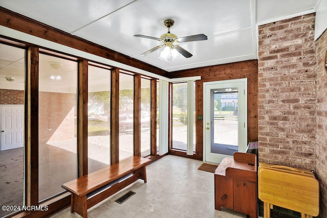 doorway to outside featuring ceiling fan and brick wall