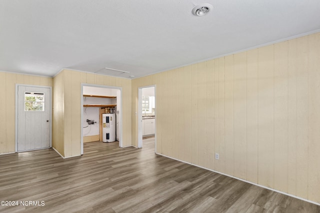 unfurnished living room with hardwood / wood-style floors, electric water heater, and wooden walls