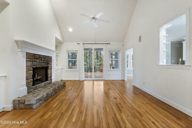 unfurnished living room with built in shelves, ceiling fan, a stone fireplace, high vaulted ceiling, and light hardwood / wood-style floors